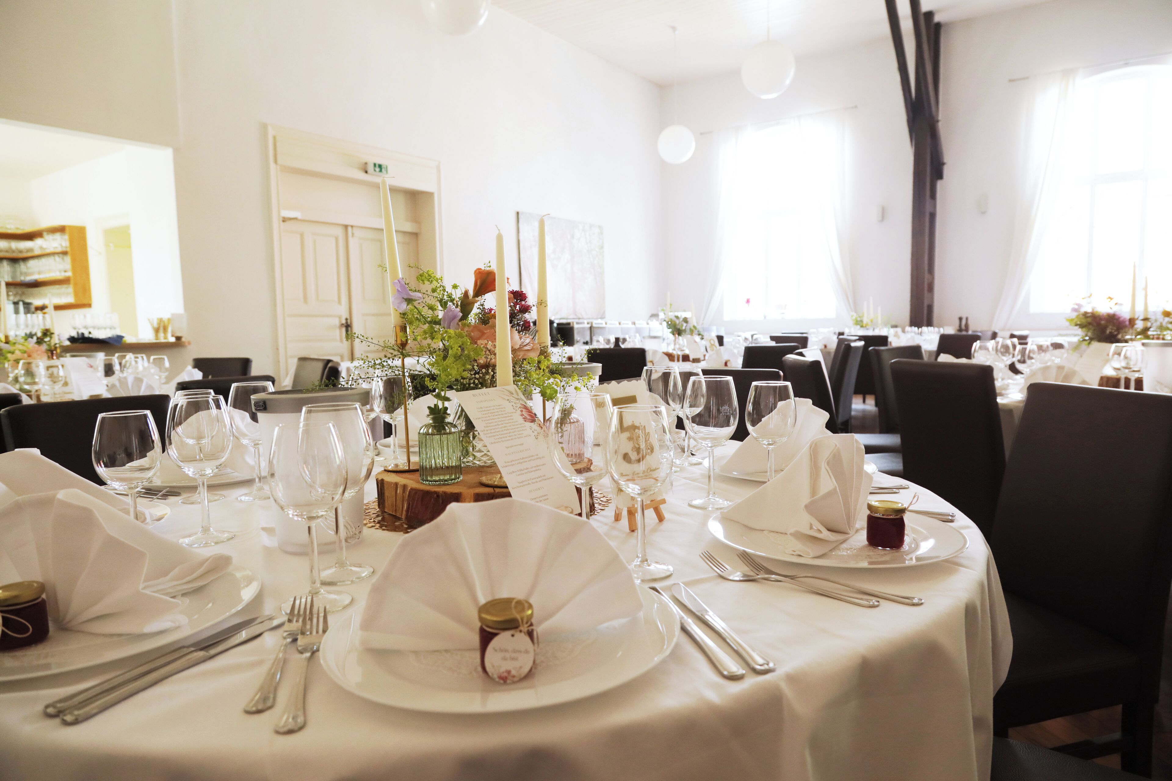 A dining area with round tables set for a meal, complete with white tablecloths, plates, cutlery, and glassware.