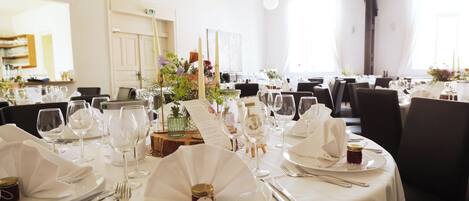 A dining area with round tables set for a meal, complete with white tablecloths, plates, cutlery, and glassware.