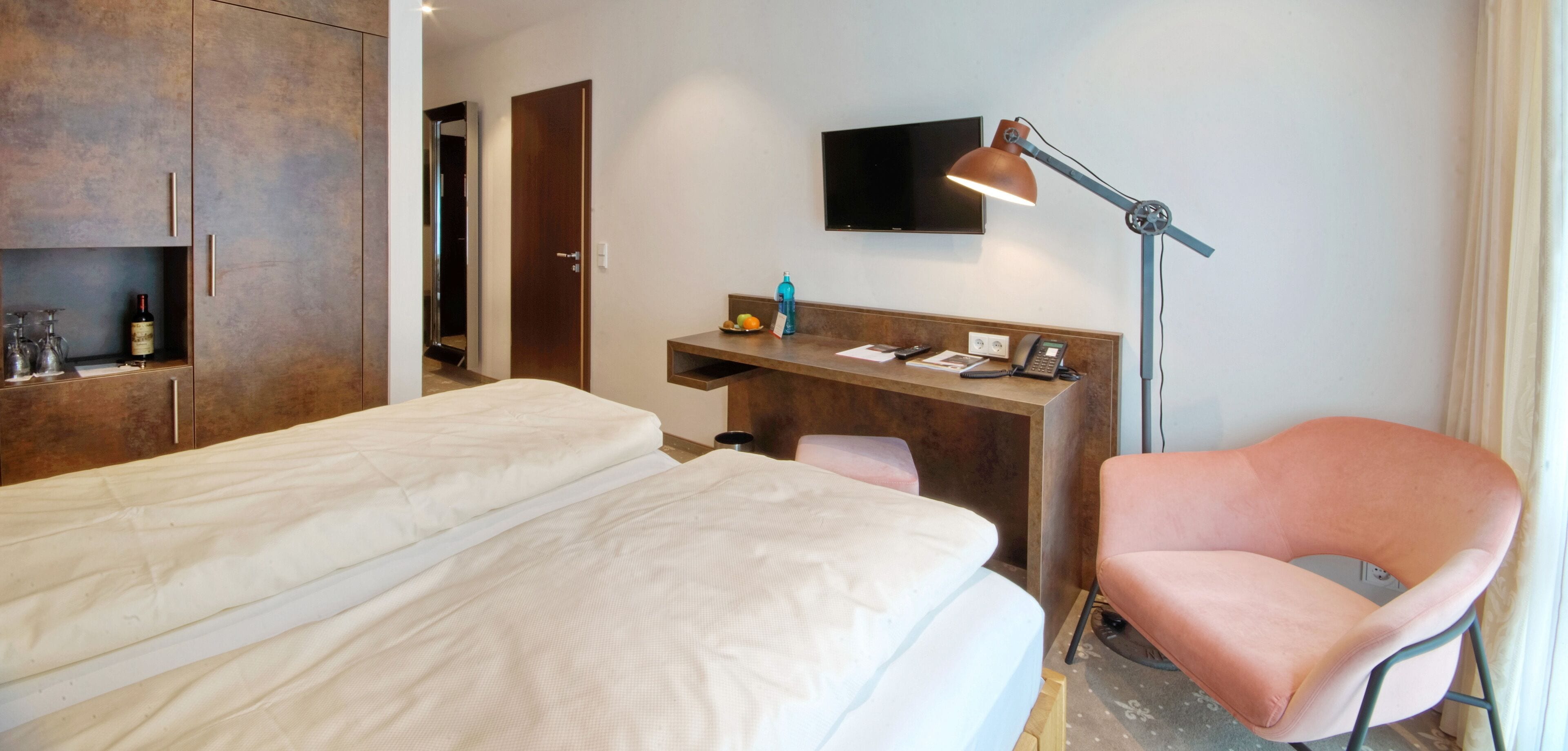 Una habitación de hotel con una cama, un escritorio con lámpara, una silla y un televisor.