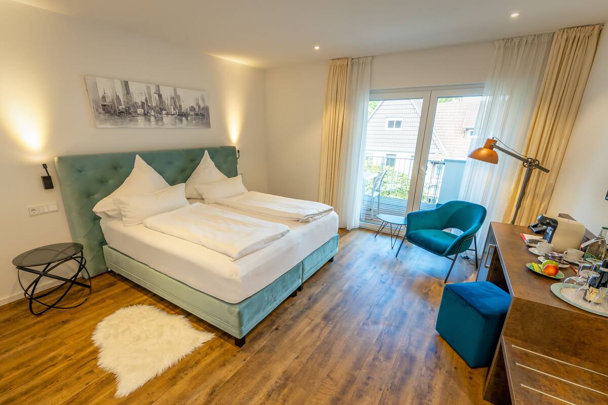 A modern hotel room with a large bed, a desk, a chair, and a view of the outside.