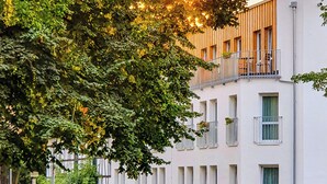 Un edificio de varios pisos con fachada blanca, numerosas ventanas y un balcón en el nivel superior.