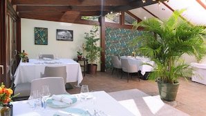 Un restaurante con terraza, manteles blancos y plantas en macetas.