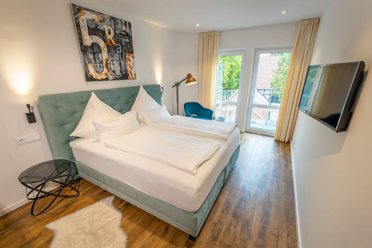 A modern hotel room with a large bed, a TV, a desk, and a balcony with a view.