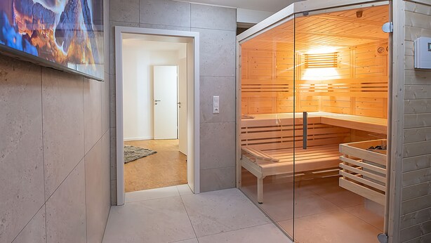 Una sauna moderna con puerta de vidrio, bancos de madera y panel de control a la vista.