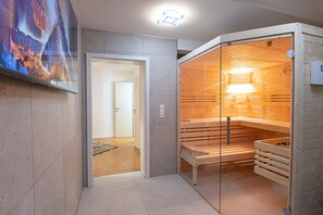 Un sauna moderne doté d’une porte en verre, de bancs en bois et d’un panneau de commande visible.