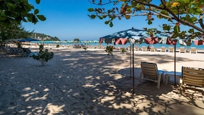 Une plage avec des transats et des parasols, un ciel dégagé et une mer calme en arrière-plan.