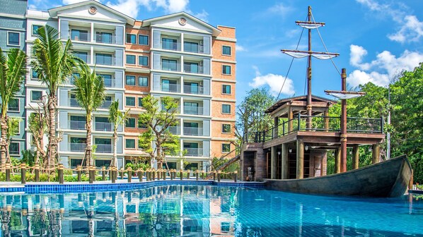 A hotel with a pool, a wooden boat, and palm trees.