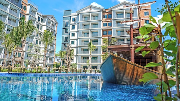 Une piscine avec un bateau en bois, entourée d’immeubles résidentiels à plusieurs étages dotés de balcons.