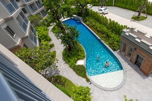 A swimming pool surrounded by greenery and a building with balconies.