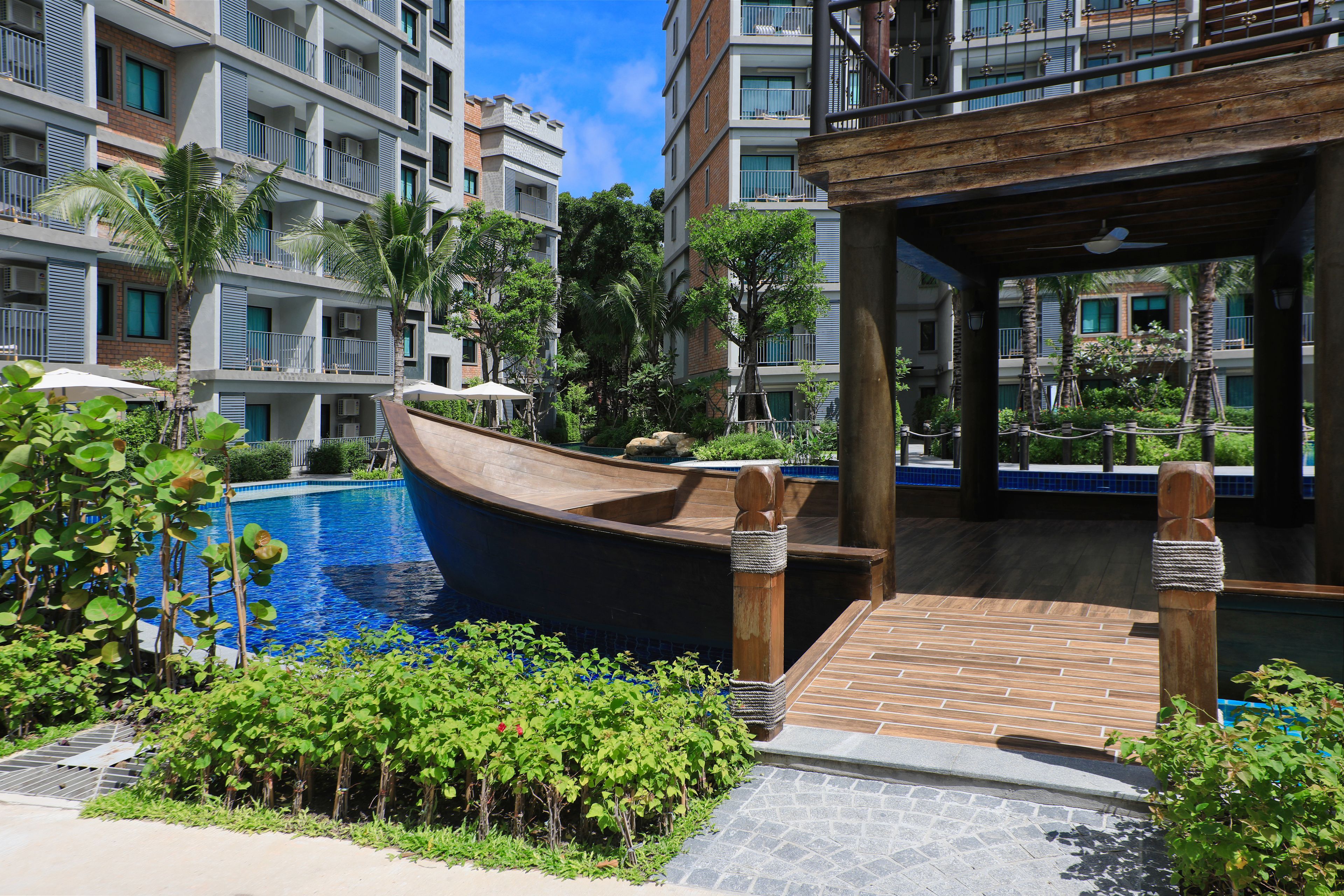 A resort pool area with a boat, wooden deck, and surrounding greenery.