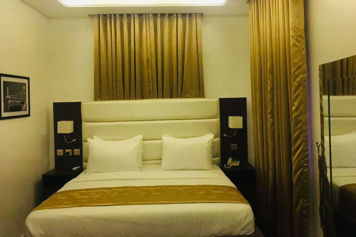 A hotel room with a bed, a bedside table, a mirror, and a curtain.