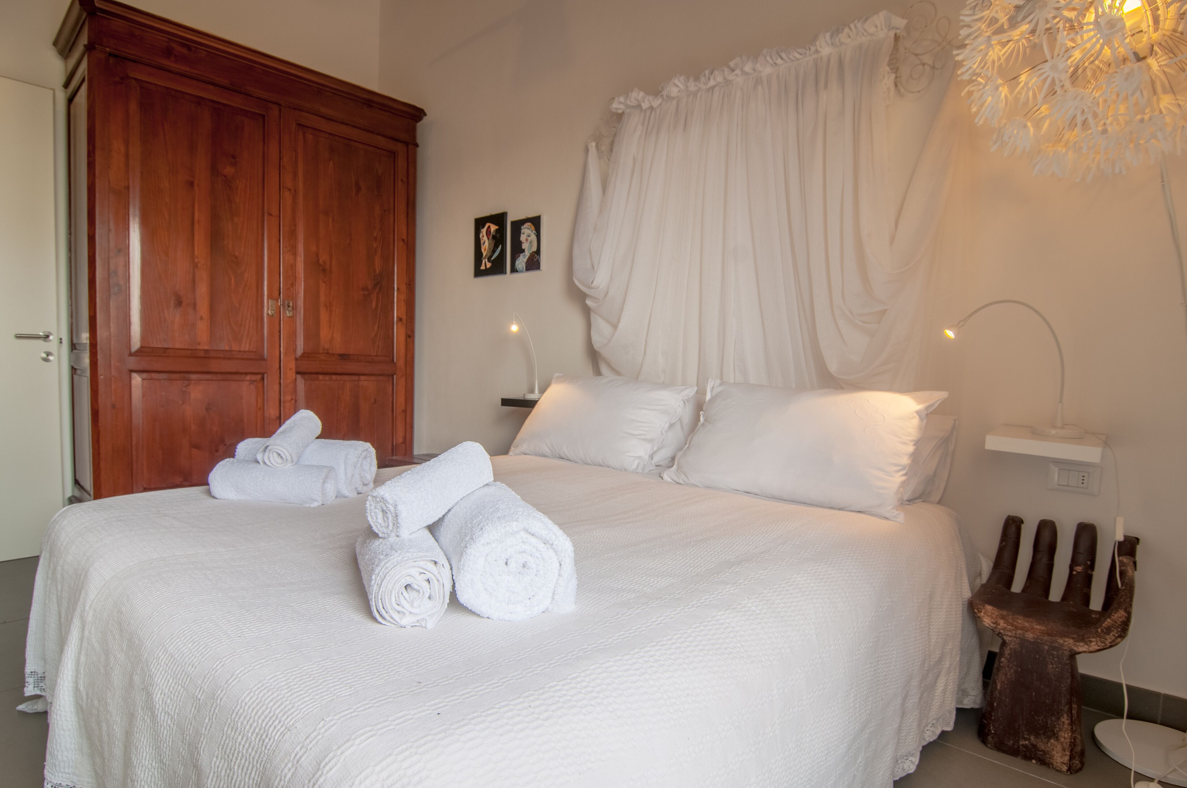 A neatly made bed with rolled white towels, a wooden wardrobe, and a bedside table with a lamp.