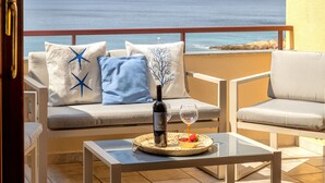 A balcony with a sofa, two armchairs, a glass table, a bottle, and a glass of wine.