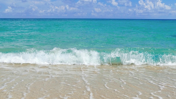 A beach with clear turquoise water and gentle waves.