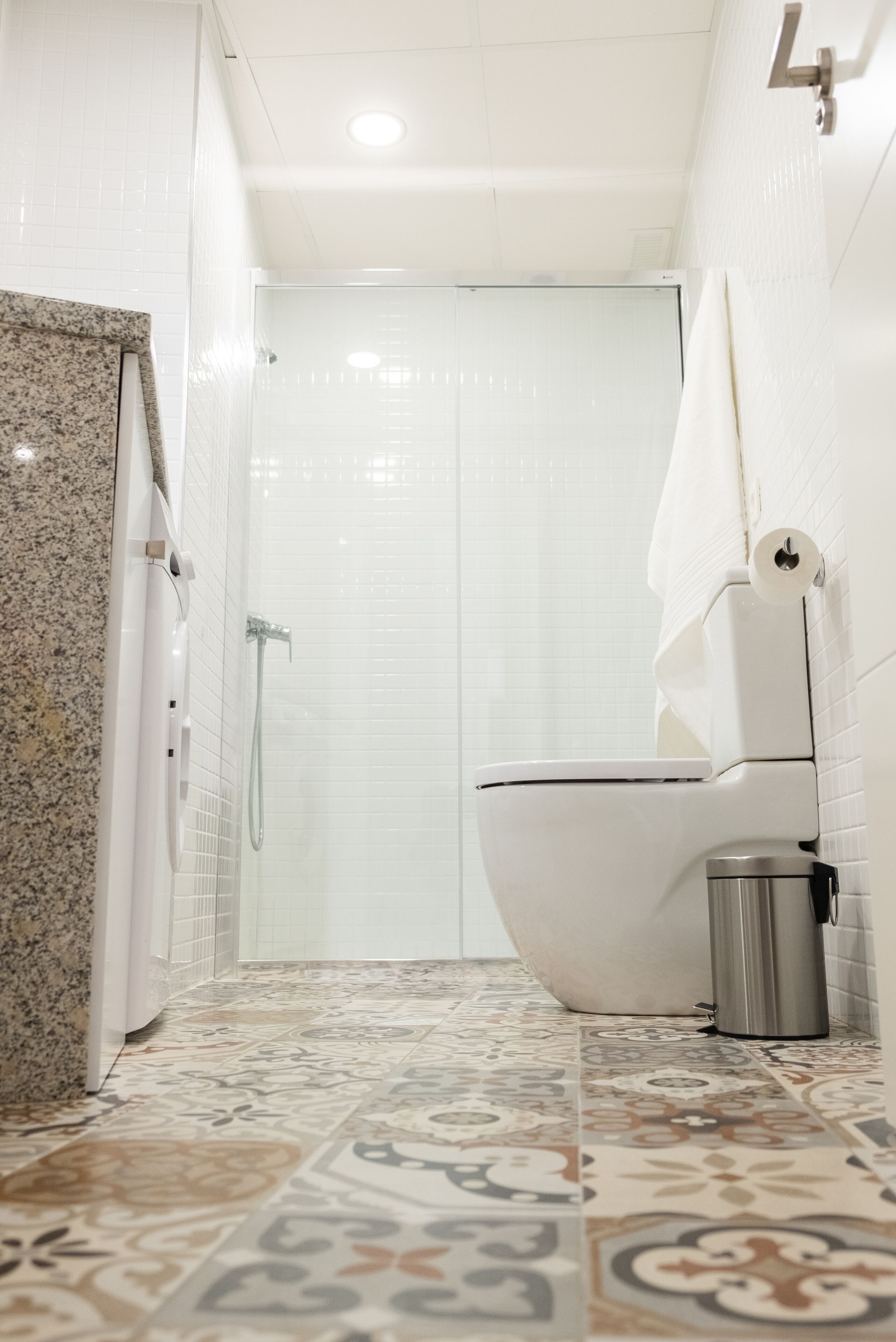 A bathroom with a shower, toilet, and a trash bin.