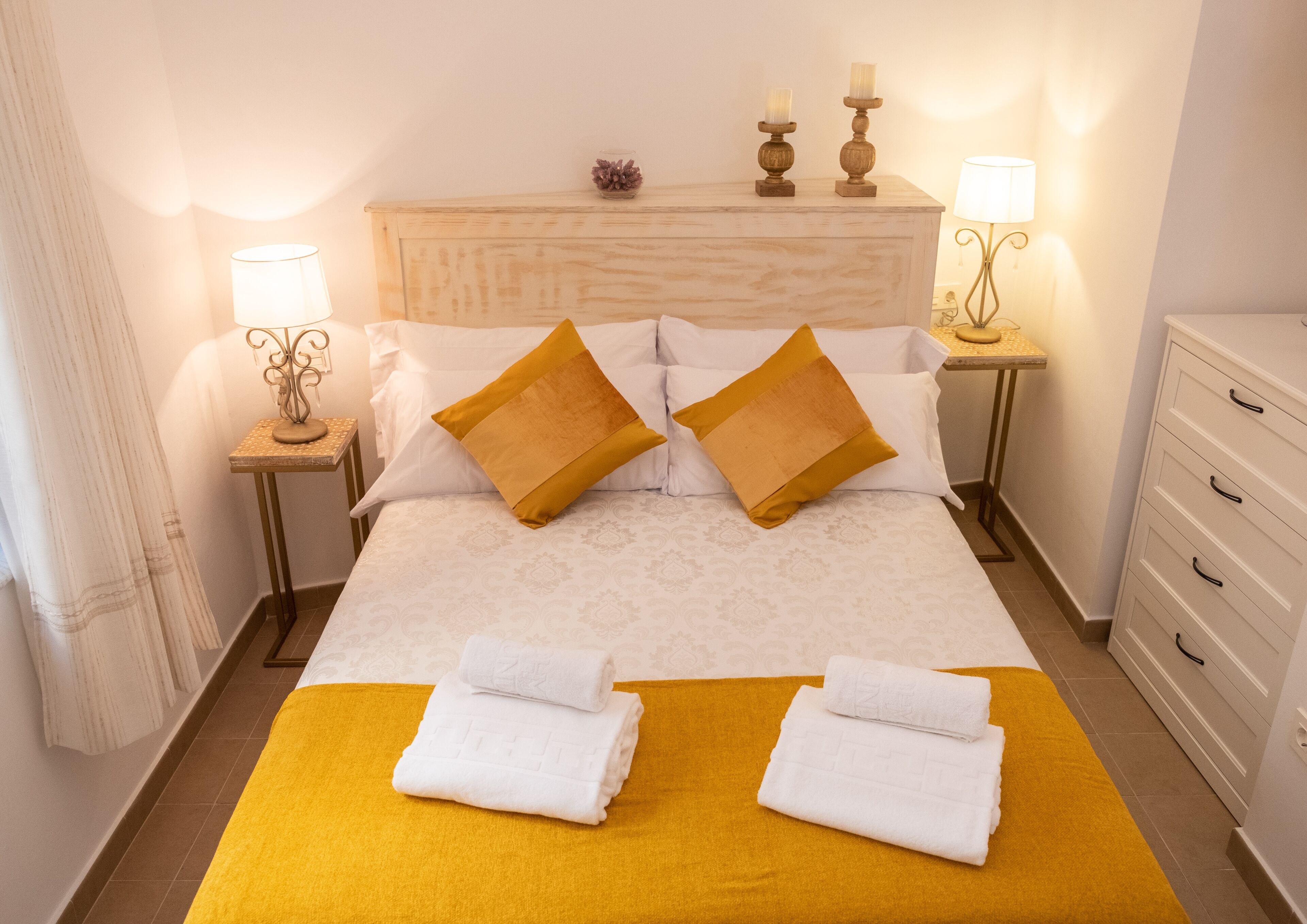 Un lit bien fait avec deux oreillers, deux tables de chevet avec des lampes, une tête de lit en bois et une commode blanche.
