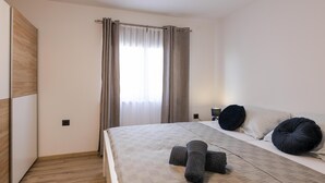 A modern bedroom with a large bed, a wooden wardrobe, and a window with curtains. - Apartments Lovric - Apt 2 (Pula)
