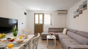 A modern living room with a sofa, a dining table with breakfast, a TV, and a window with curtains. - Apartments Lovric - Apt 2 (Pula)