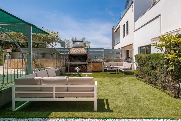 A modern outdoor patio with a white sofa, a stone barbecue, and a small table.
