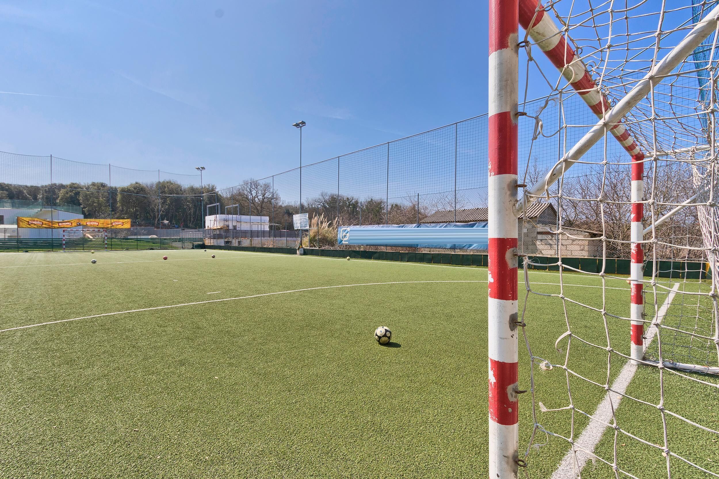 Un campo de fútbol con un arco, rodeado de una valla y árboles al fondo.