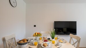 A breakfast setup with a variety of foods and drinks on a table, a clock on the wall, and a TV mounted on the wall. - Apartments Lovric - Apt 2 (Pula)