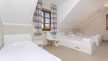 Une chambre moderne et bien éclairée, avec trois lits, un bureau et une fenêtre avec des rideaux.