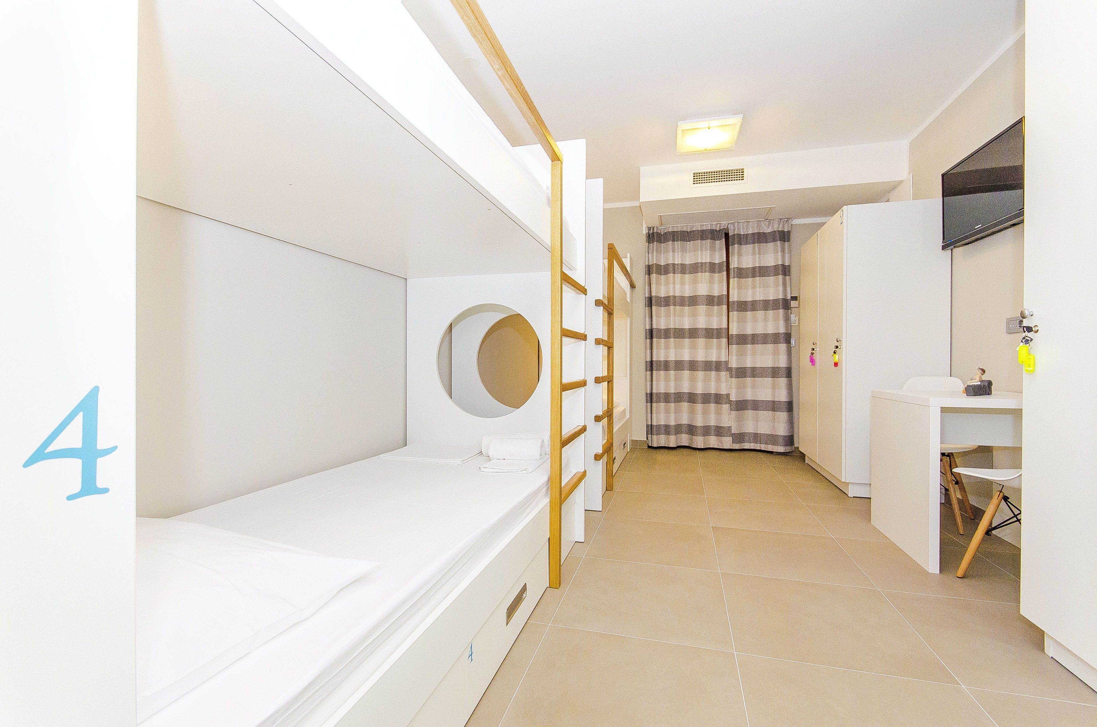Habitación de hotel con literas, un escritorio pequeño, una silla, baño con espejo y cortina de ducha.
