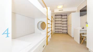 Habitación de hotel con literas, un escritorio pequeño, una silla, baño con espejo y cortina de ducha.