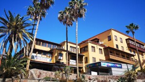 Un edificio de varios pisos con fachada amarilla, palmeras y un letrero que dice 'Happy Park'.