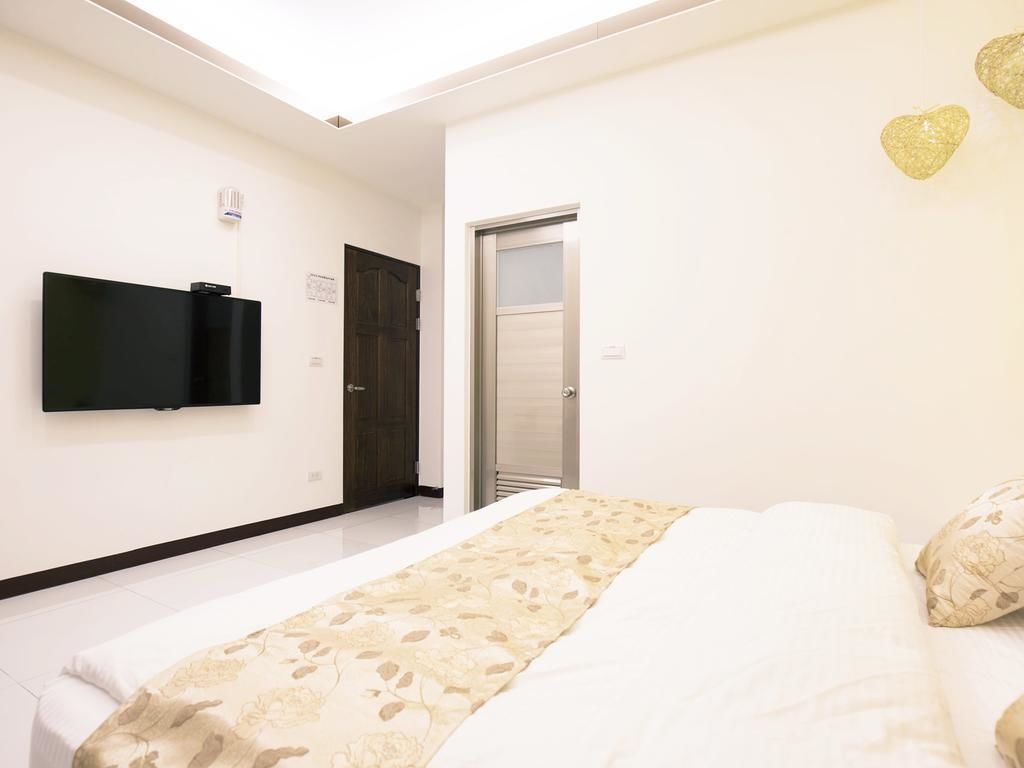 A bedroom with a bed, a television mounted on the wall, and a door leading to another room.