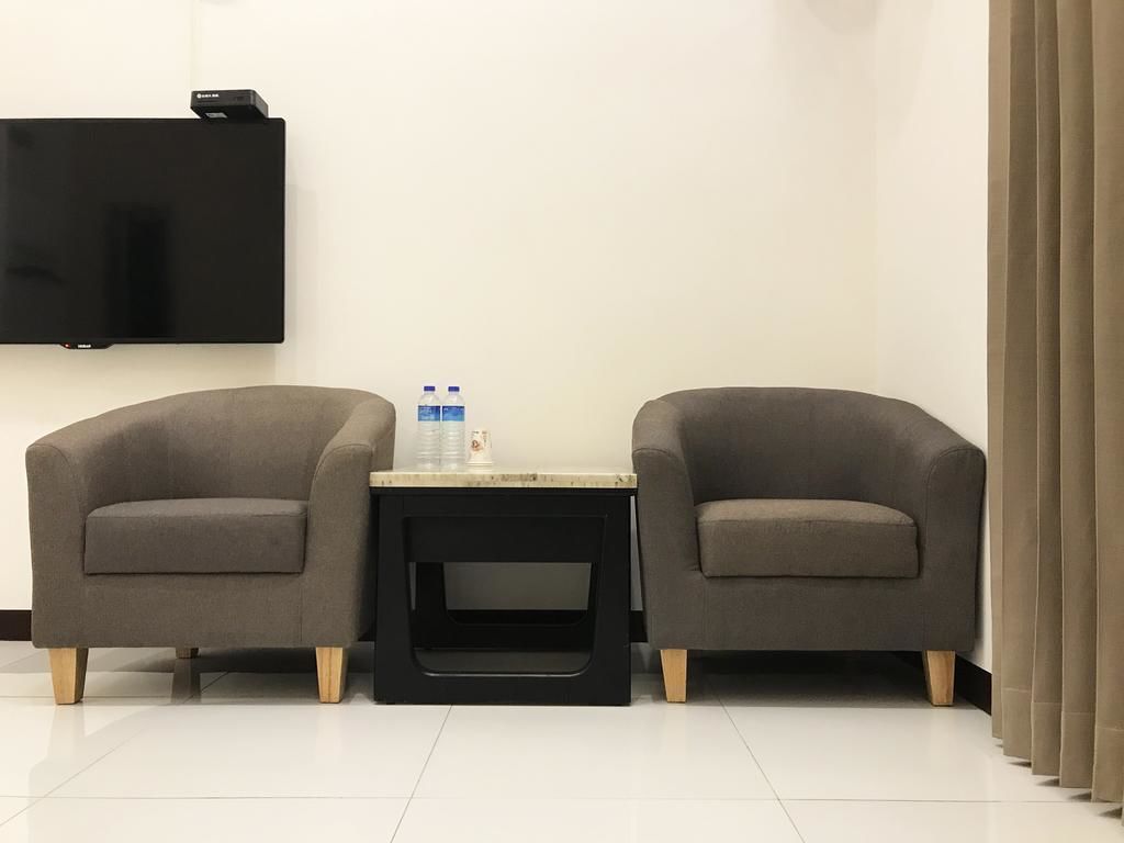 A room with two grey armchairs, a small table with water bottles, a flat-screen TV mounted on the wall, and a curtain on the right side.