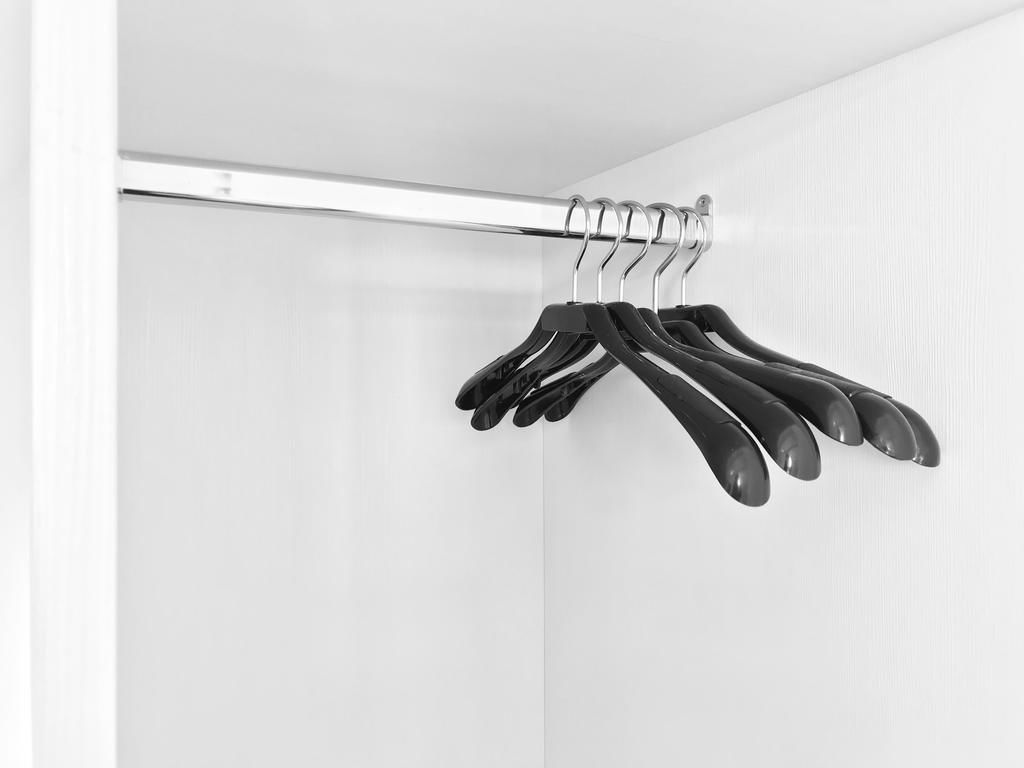 Un placard avec une tringle métallique sur laquelle sont accrochés plusieurs cintres noirs.