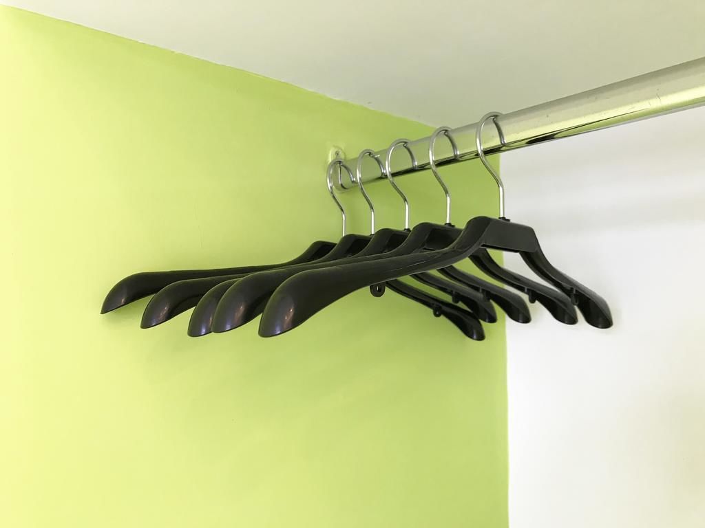 A metal curtain rod with black hangers against a lime green wall.