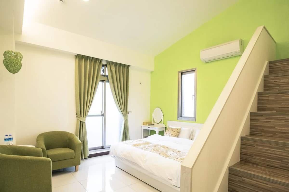 Een slaapkamer met een bed, een stoel, een raam en een trap.