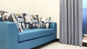 A blue sofa with patterned cushions, a grey curtain, and a white tiled floor.