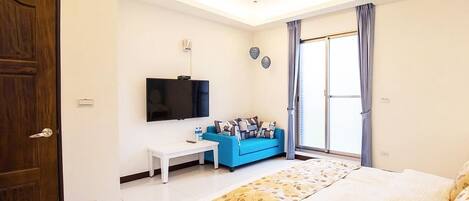 Un dormitorio con cama, televisión, sofá y ventana con cortinas.