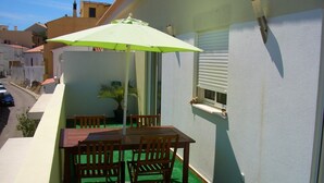 En balkon med et bord, stole, en grøn parasol og en potteplante.