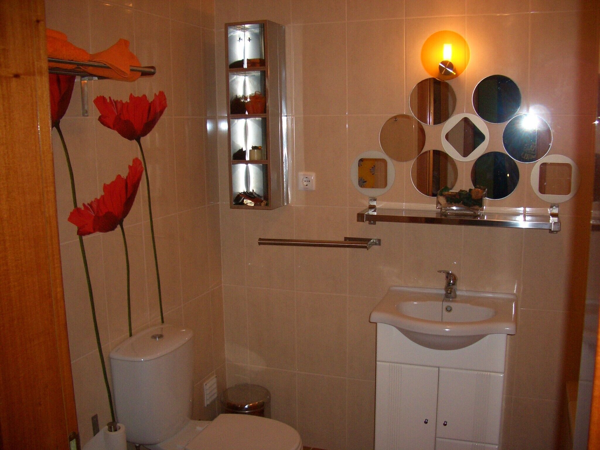 Une salle de bain comprenant des toilettes, un lavabo et un miroir mural agrémenté de plusieurs petits miroirs ronds.