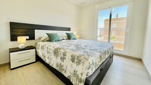 A bedroom with a bed, nightstands, and a window with a view of buildings. - Apartamento Azul (Villamartin) (Orihuela Costa)