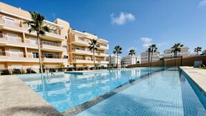 A swimming pool with clear blue water, surrounded by a tiled deck. - Apartamento Azul (Villamartin) (Orihuela Costa)
