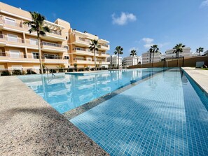 A swimming pool with clear blue water, surrounded by a tiled deck.