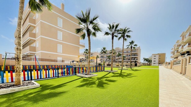 A residential area with a playground, palm trees, and modern apartment buildings.