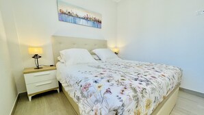 Un lit bien fait, avec une couvre-lit à motifs floraux, une tête de lit et deux lampes de chevet.