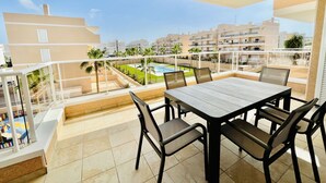 A balcony with a table and chairs, overlooking a swimming pool and residential buildings. - Apartamento Azul (Villamartin) (Orihuela Costa)