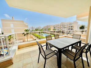 A balcony with a table and chairs, overlooking a swimming pool and residential buildings.