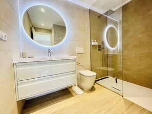 A modern bathroom with a glass shower enclosure, a white vanity with a round mirror, and a toilet.