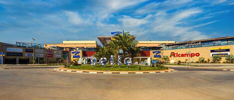 A commercial area with a central roundabout, surrounded by various businesses including a pharmacy, a fast-food restaurant, and a pizzeria.