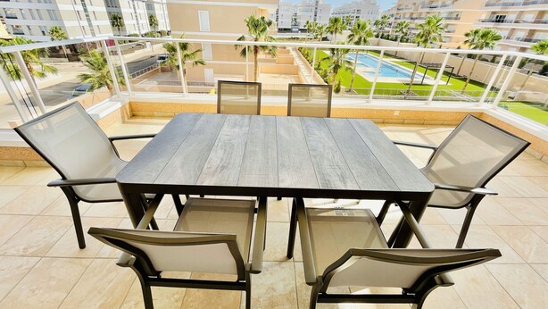 Une terrasse avec une table et des chaises en bois, une piscine et une vue sur les bâtiments environnants.