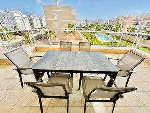 Een terras met een houten tafel en stoelen, een zwembad en uitzicht op omliggende gebouwen.