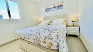 A bedroom with a bed, two bedside tables, a nightstand, a window, and a painting on the wall.